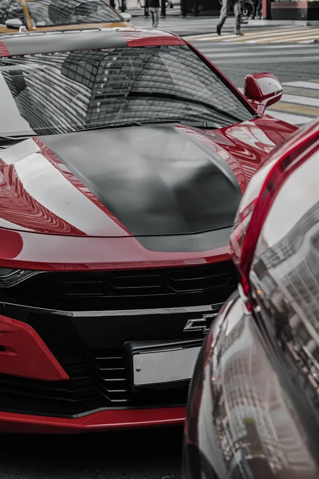Red muscle car with white racing stripes and a satin black hood