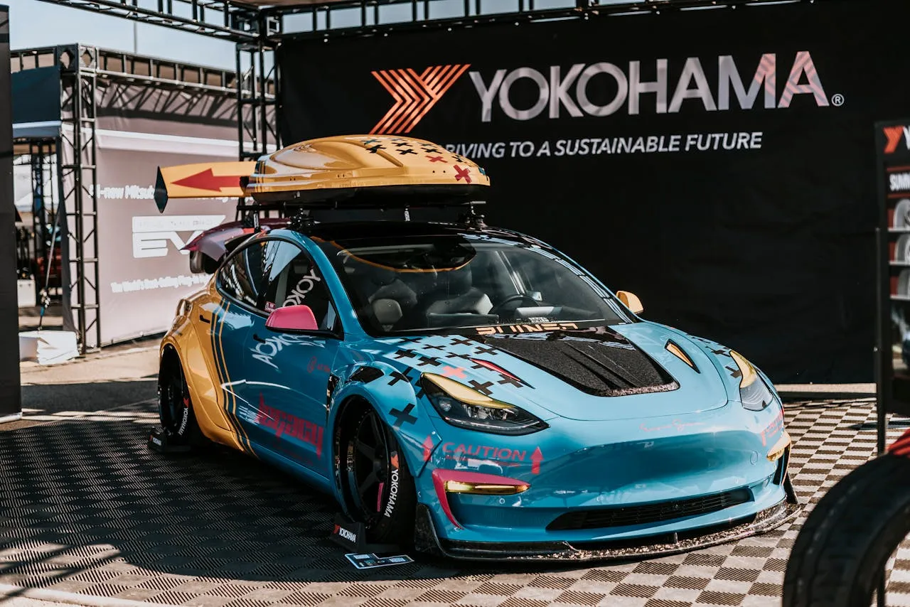 Blue and yellow widebody electric sedan with racing stripes and decals at a car show